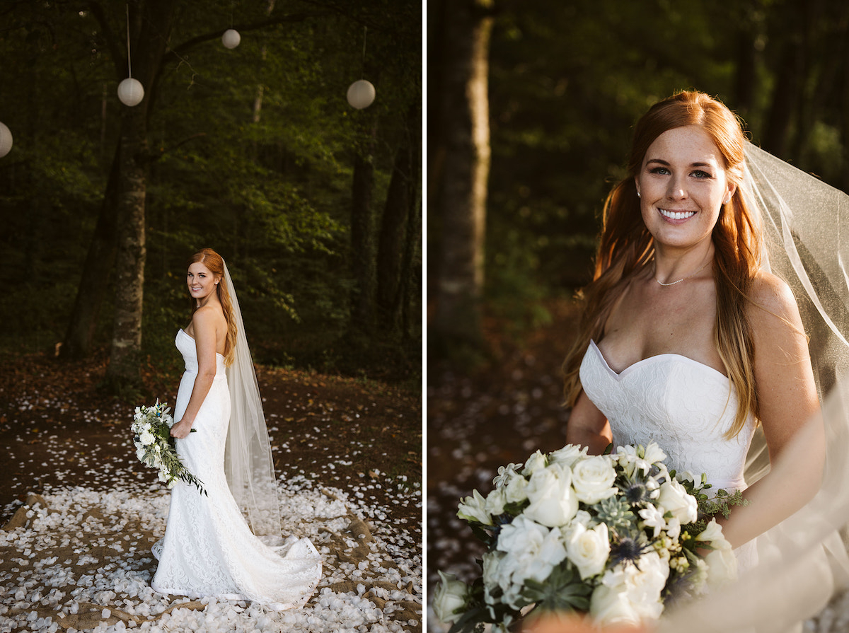 bride stands on a bed of white petals beneath tall green trees hung with white paper lanterns. she holds large white bouquet