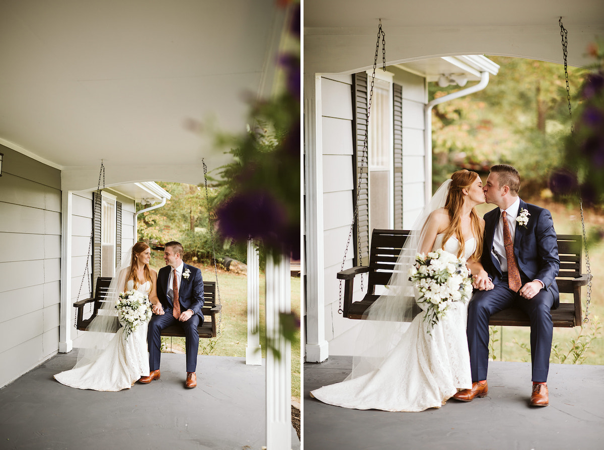 bride and groom hold hands and kiss as they sit together on a wooden porch swing