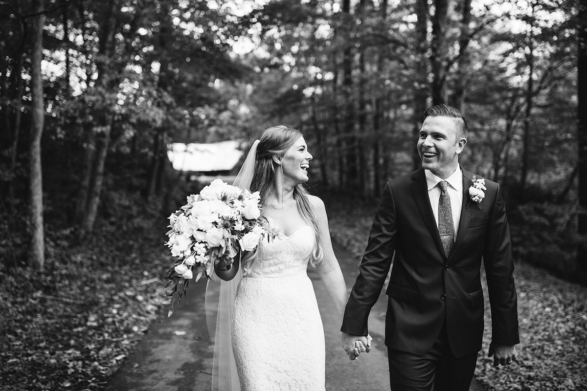 bride and groom hold hands and laugh as they walk down a paved driveway