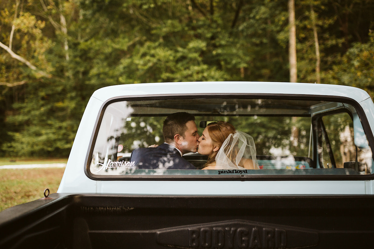 Bride and groom sit in a light blue antique Ford pickup truck kissing