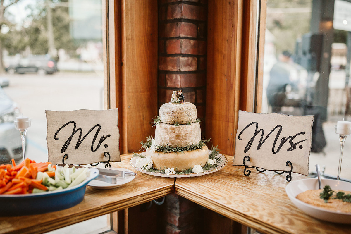 Small tabletopMr. and Mrs. signs sit on either side of a stack of 3 wheels of cheese made to look like a wedding cake.