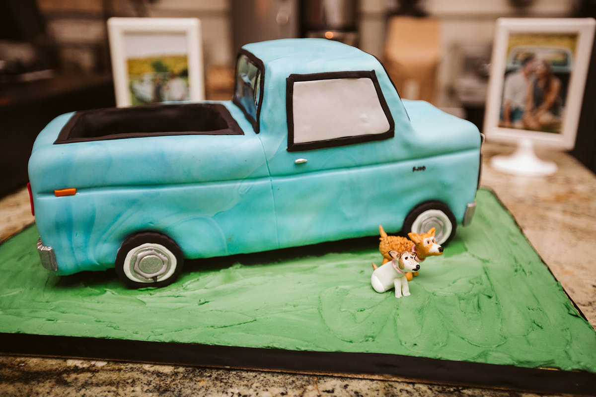 cake shaped like and decorated like a blue Ford pickup truck. Two frosting pups sit next to it.