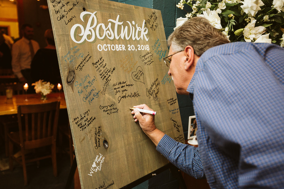 man signs a wooden board to leave a personal message for the couple