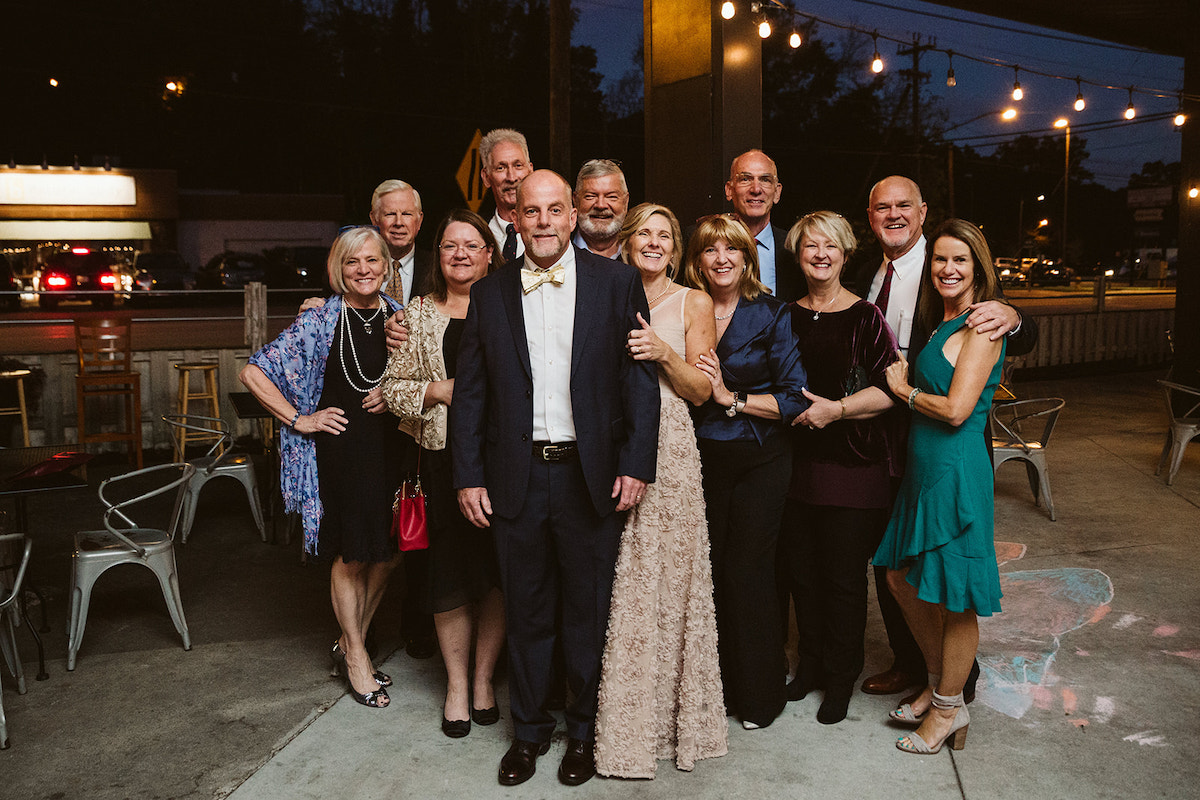 Wedding guests in formal attire pose for a photo on the patio at The Daily Ration