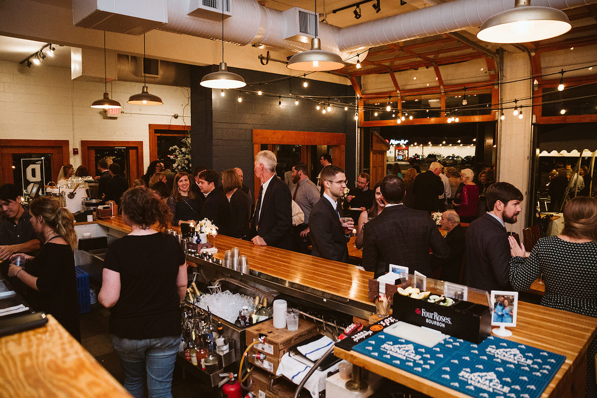 people gather at the bar inside The Daily Ration. The exterior garage doors are wide open.