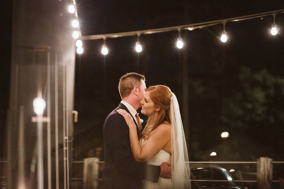 bride and groom dance under white patio lights at The Daily Ration during their wedding reception