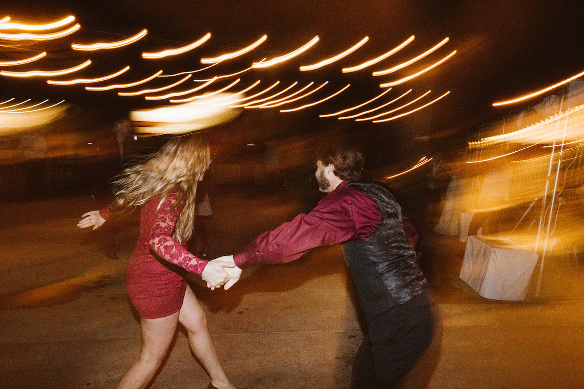 man in red shirt and dark vest and woman in red lacy dress dance together