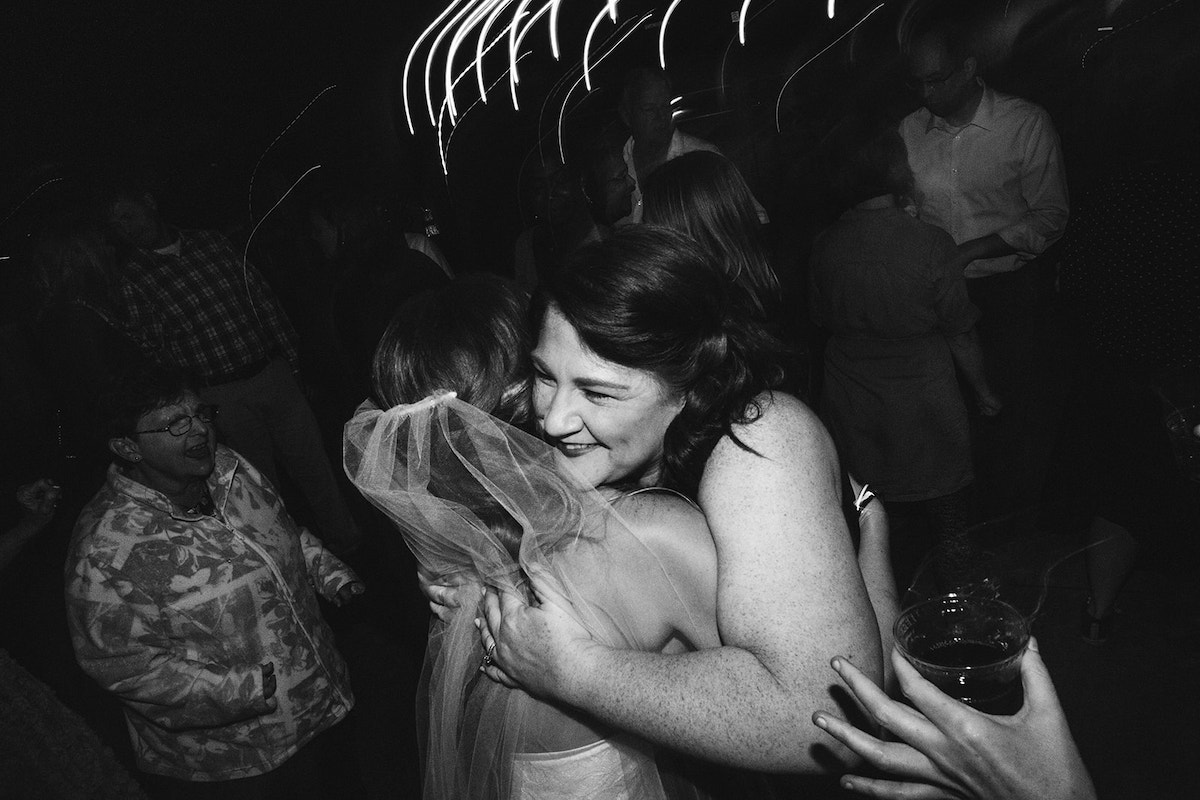 bride hugs a friend as guests dance near them