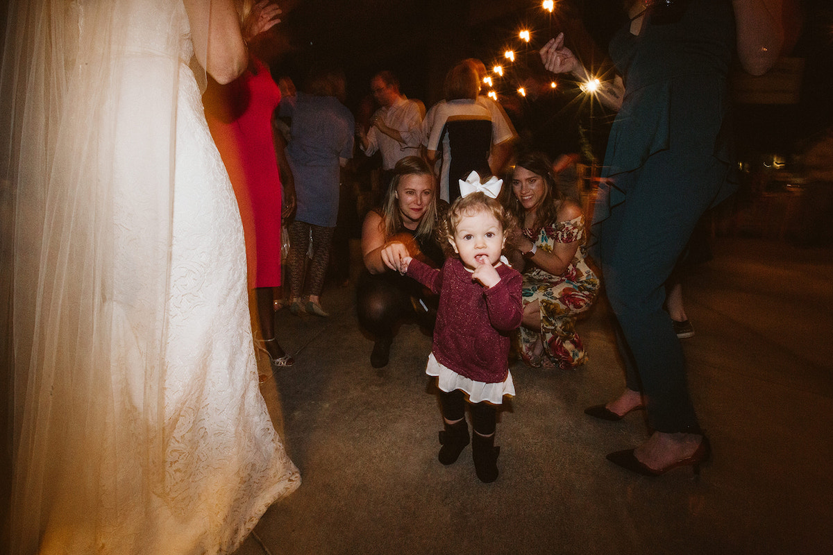 toddler girl with large white bow walks toward bride