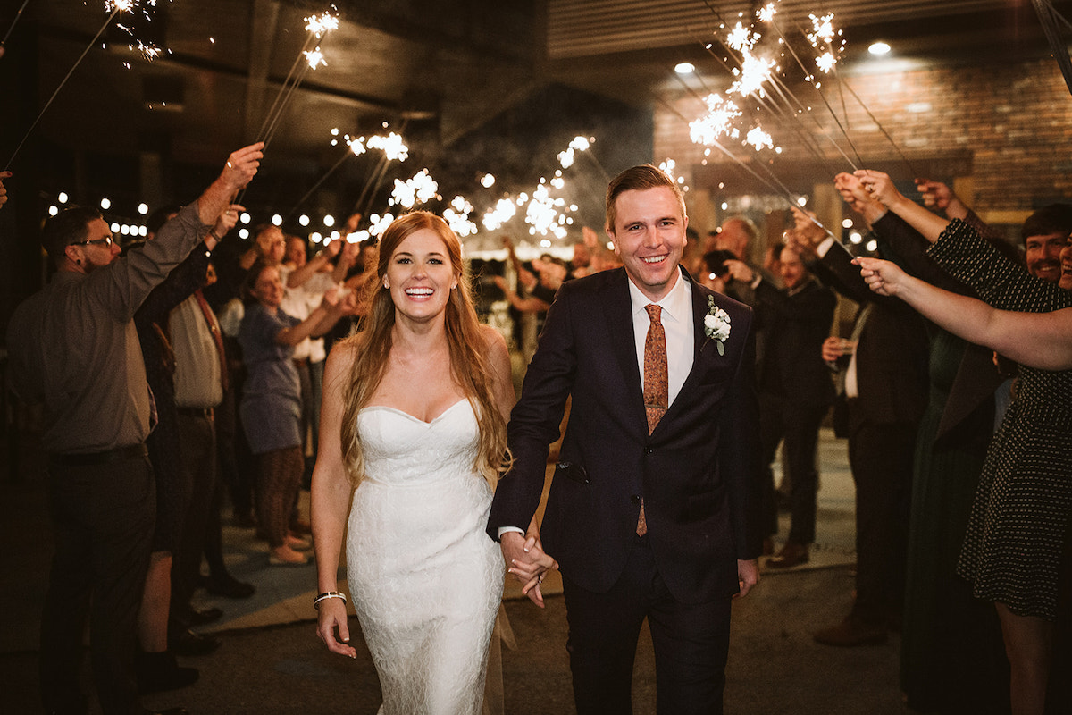 bride and groom hold hands and walk through sparkler tunnel as they leave their wedding reception at The Daily Ration