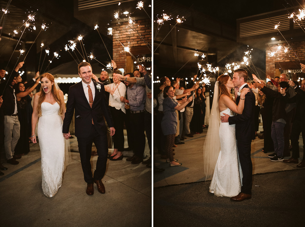 bride and groom kiss beneath sparklers as guests cheer for them.