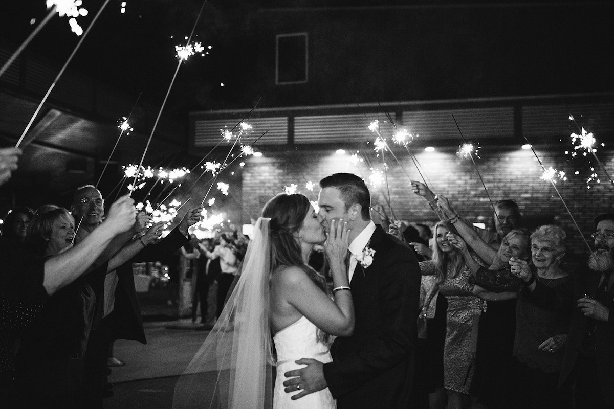 bride and groom kiss beneath sparklers as guests cheer for them.