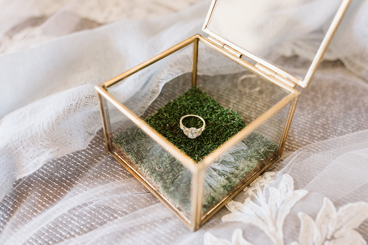 diamond engagement ring rests on a green square inside a glass box