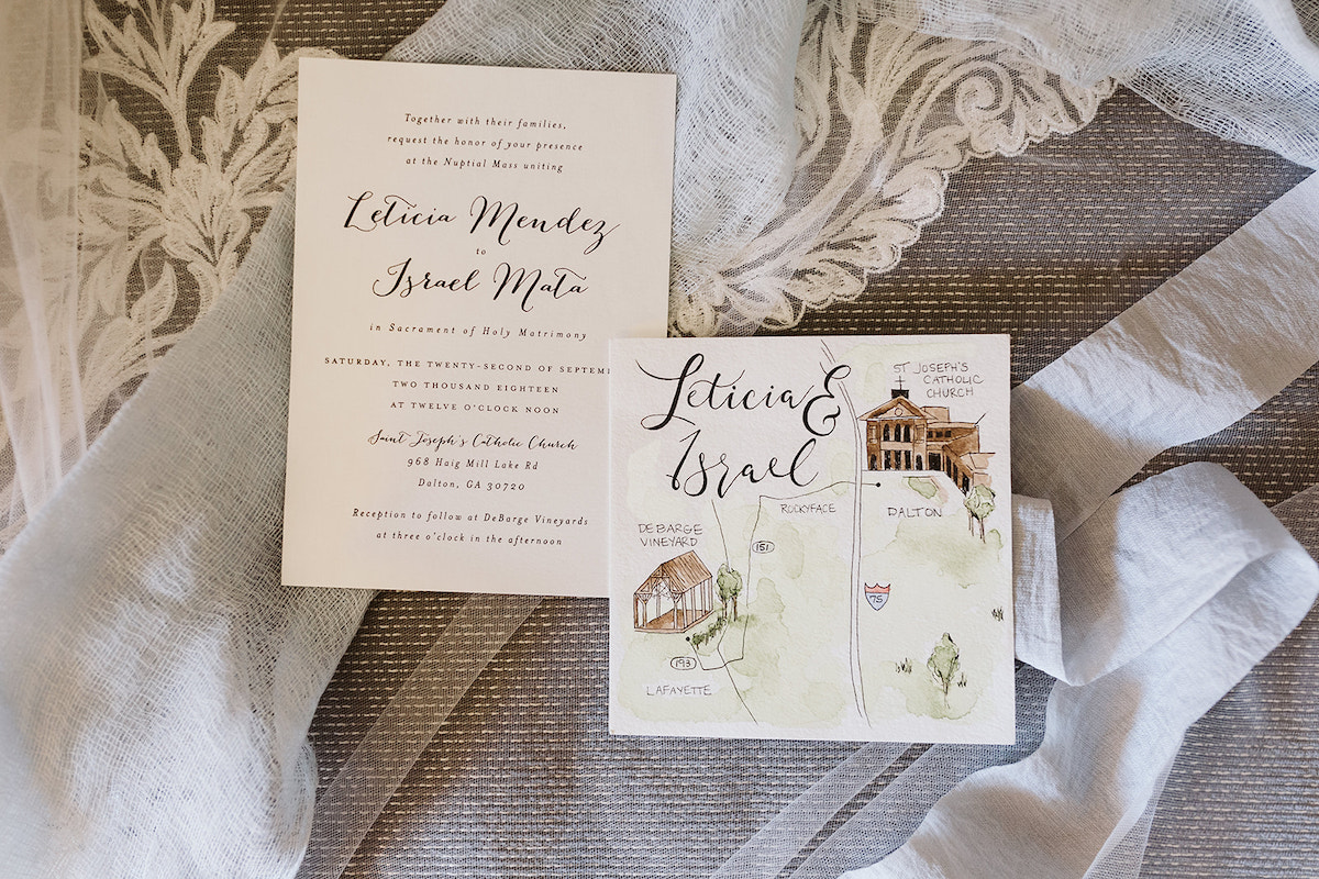 wedding invitation and watercolor map of ceremony and reception sites sit on brides tulle veil