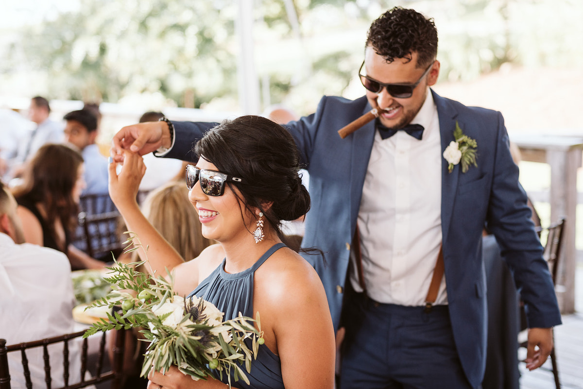 bridesmaid and groomsman wear dark sunglasses, he has a cigar in his teeth