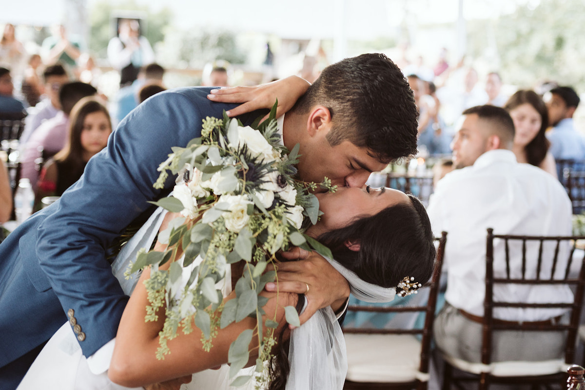 groom dips bride and kisses her while guests watch