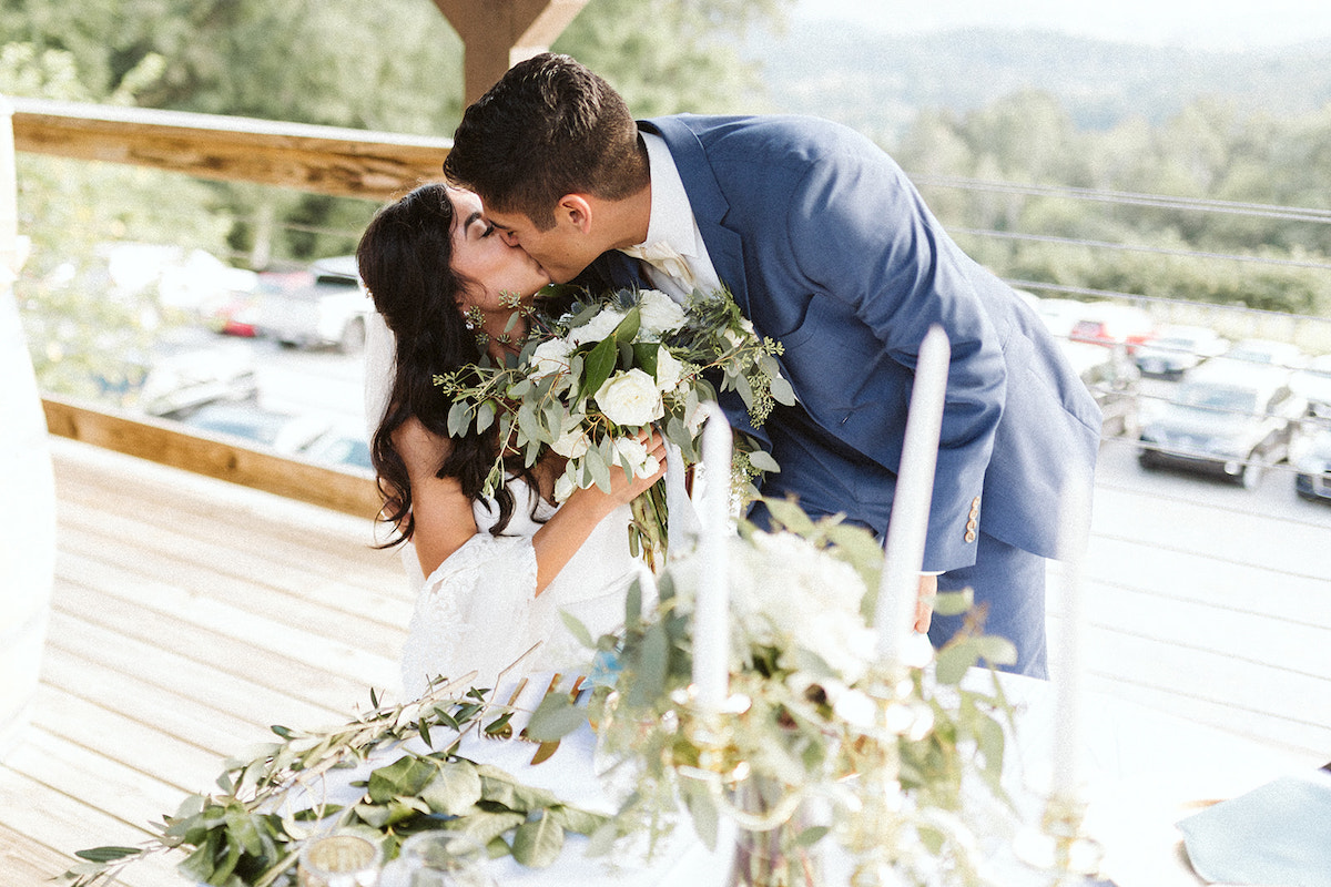 groom bends over and kisses his seated bride