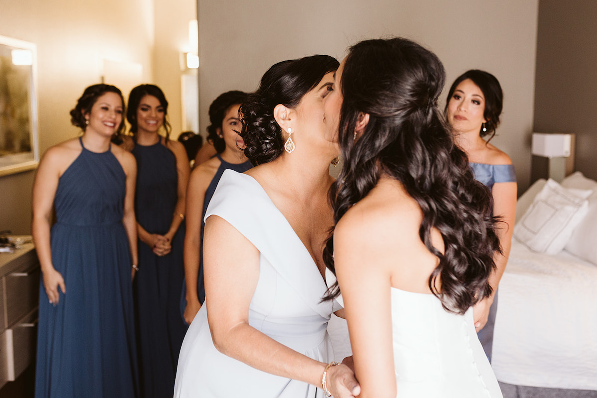mother kisses bride while bridesmaids watch