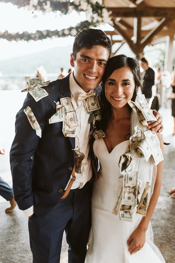 Bride and groom smile. They each have dollar bills pinned to their clothes from the Dollar Dance