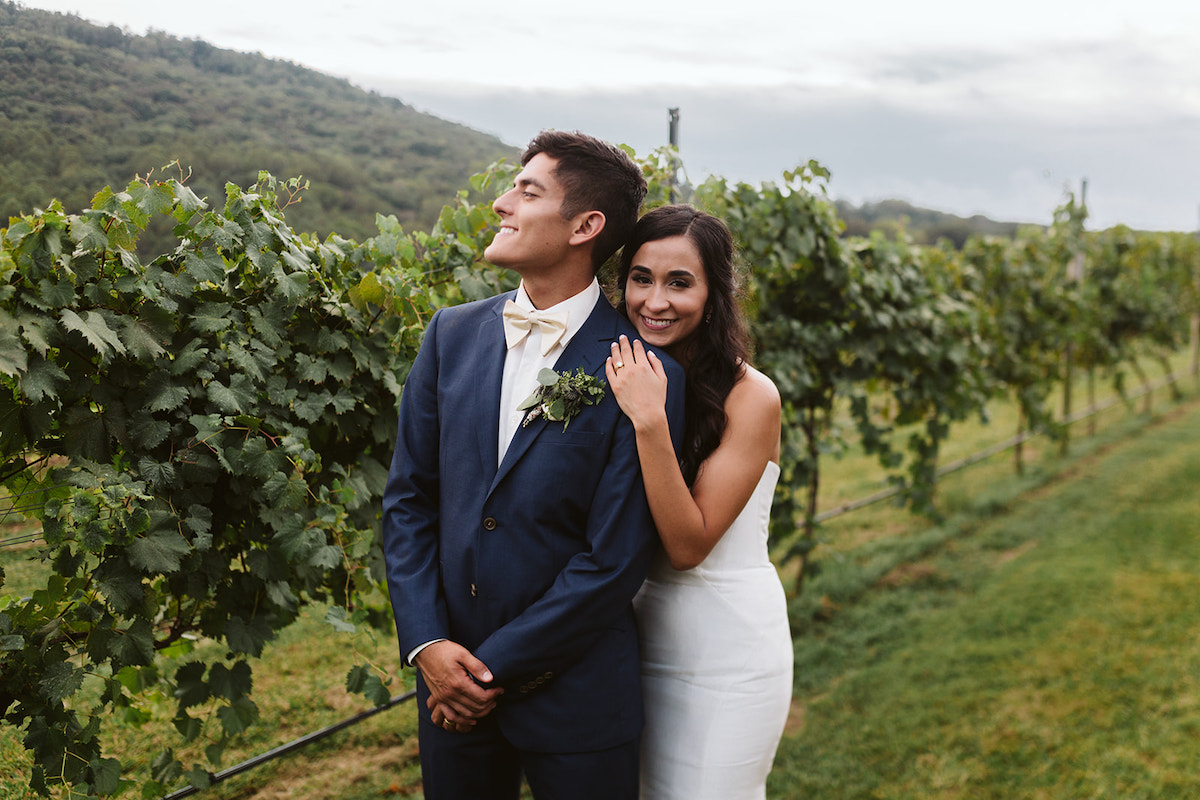 bride and groom cuddle and smile next to a vine of grapes at their DeBarge Vineyard wedding reception