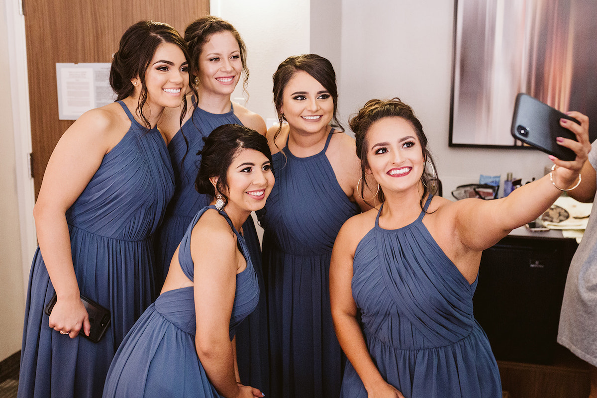 bridesmaids in cornflower blue halter dresses gather while one woman takes a selfie