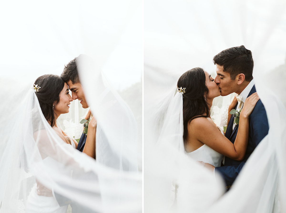 bride and groom kiss as veil swirls around them