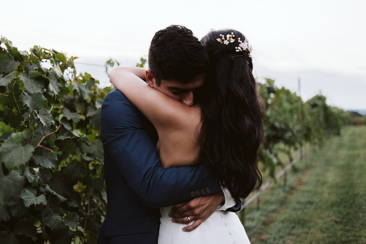 groom hugs bride next to a row of grape vines