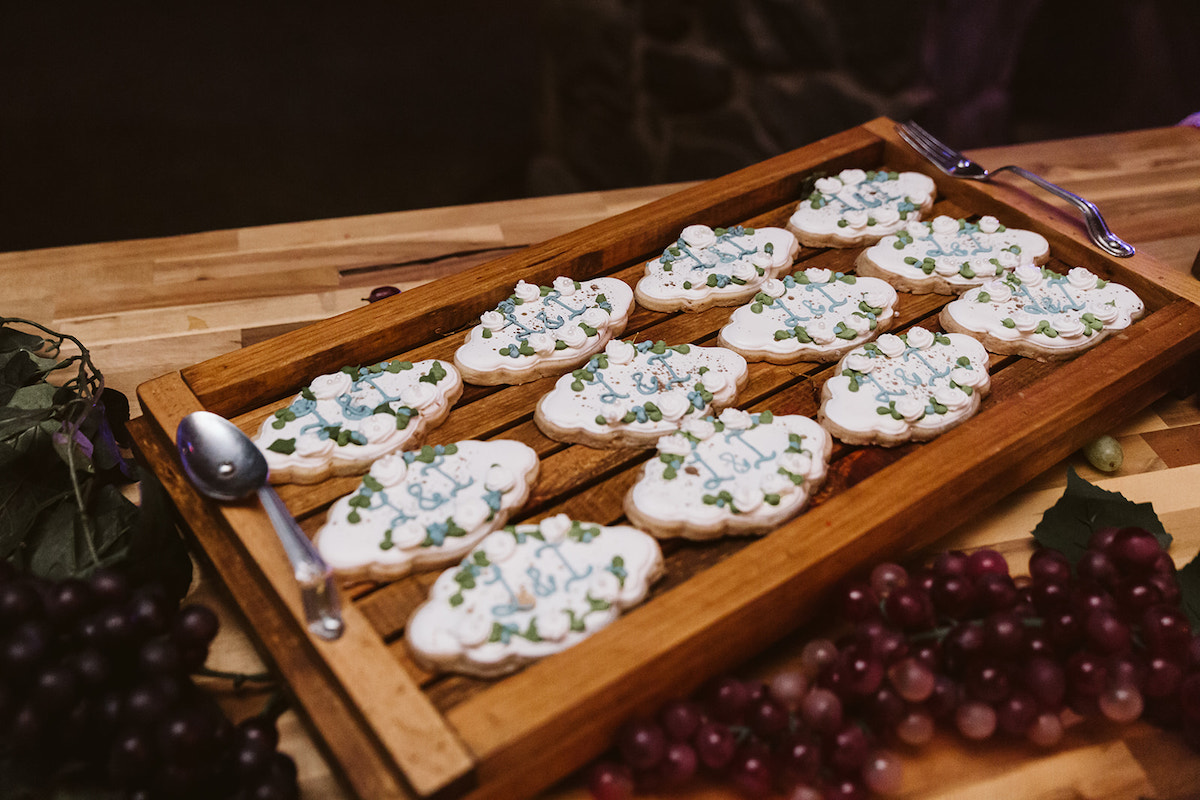 sugar cookies decorated with bride and groom initials on a platter next to vines of grapes