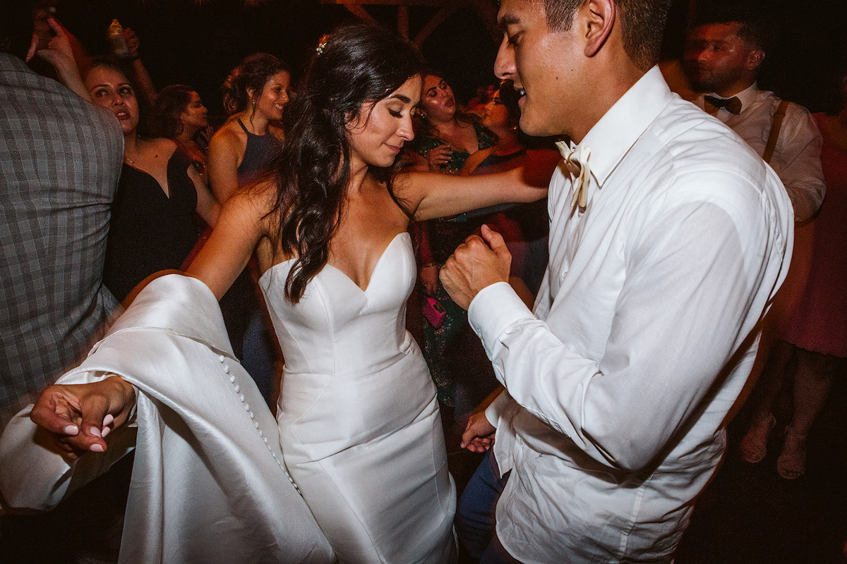 bride and groom dance together with friends around them. She holds her dress train over one arm.