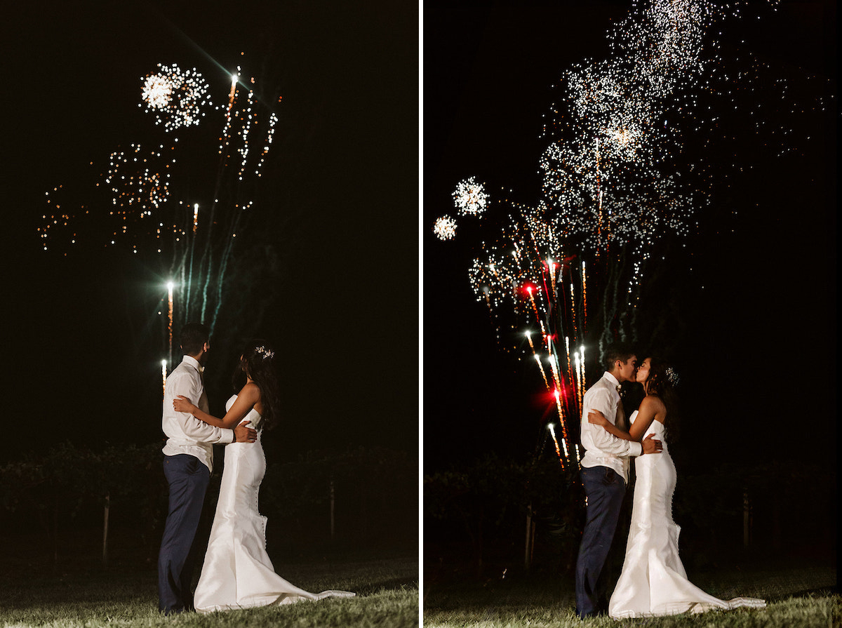 bride and groom kiss as fireworks explode in the dark sky overhead