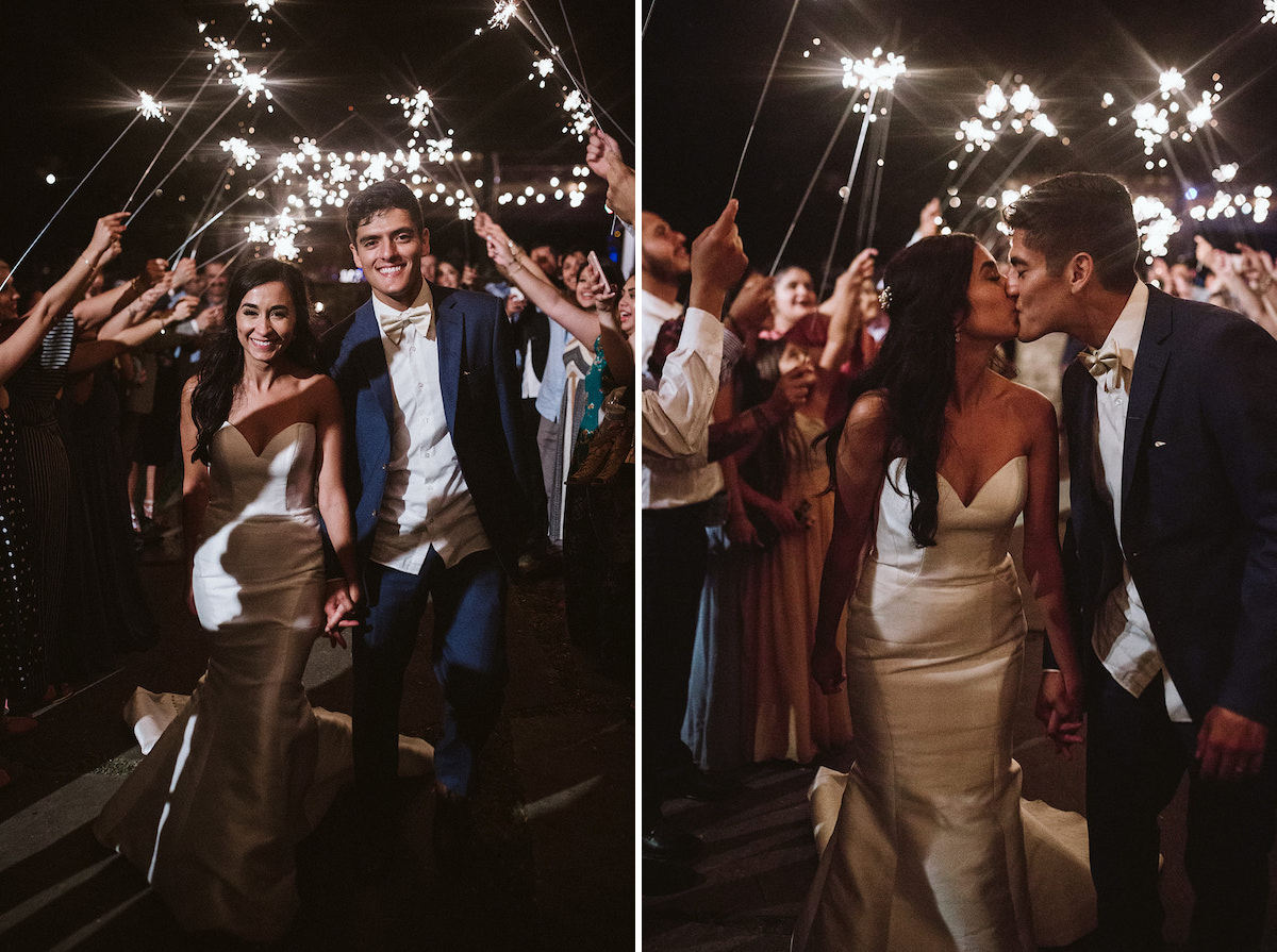 Bride and groom smile and hold hands as they walk through sparkler tunnel