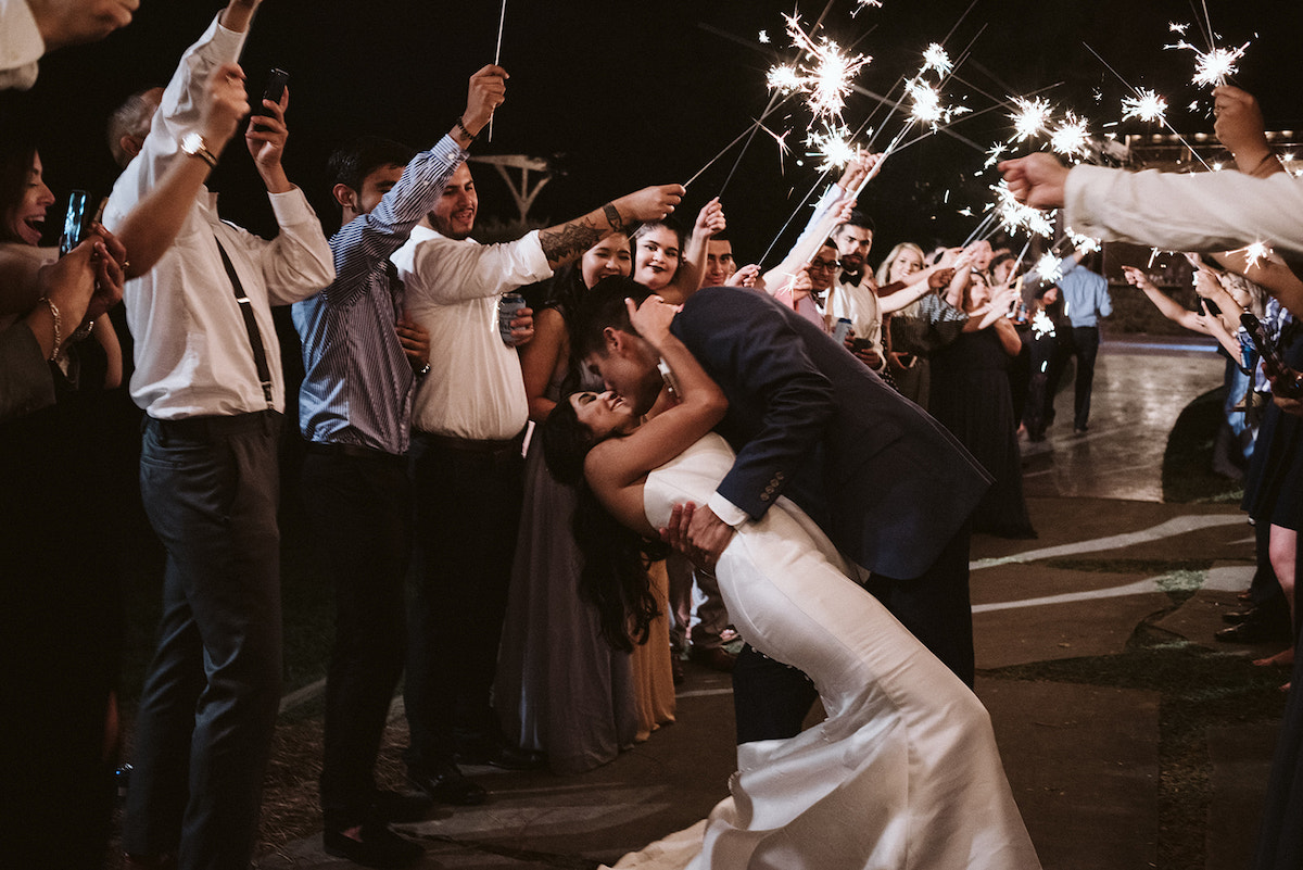 groom dips bride low as friends and family hold sparklers overhead
