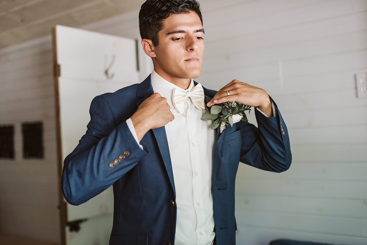 groom straightens his blue suit coat over his white shirt