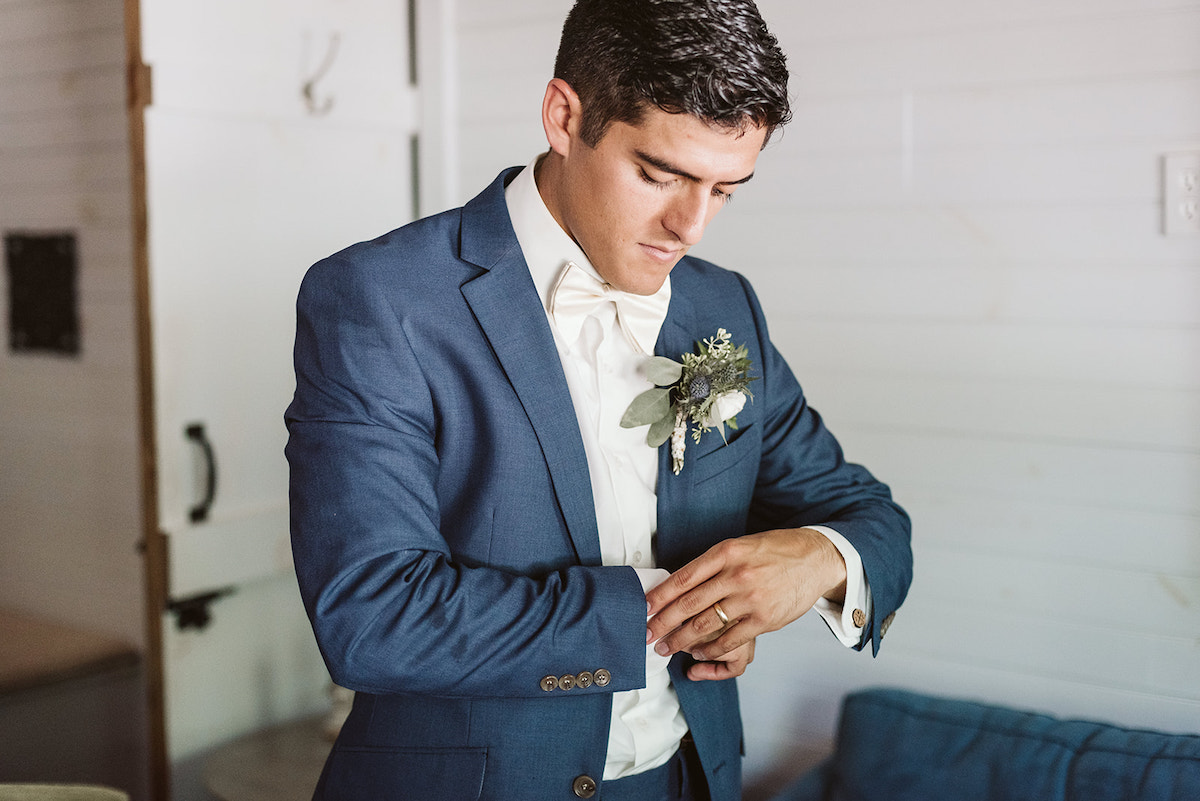 groom straightens shirt cuffs under his cornflower blue suit coat