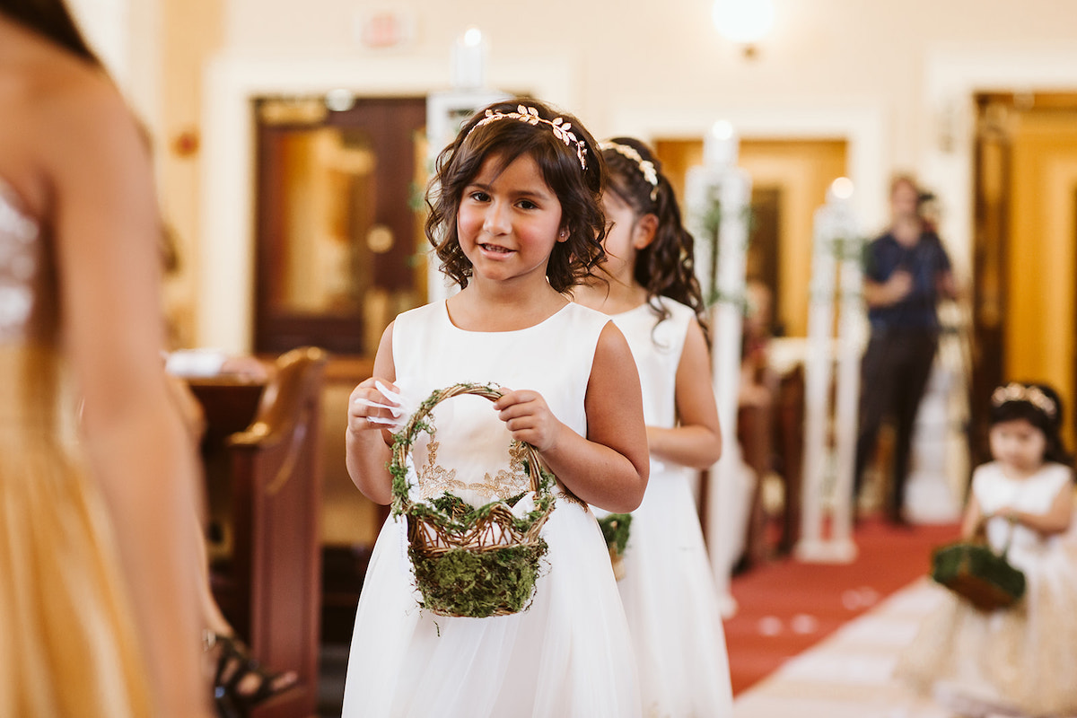 flower girls drop pedals along white runner while wedding guests smile