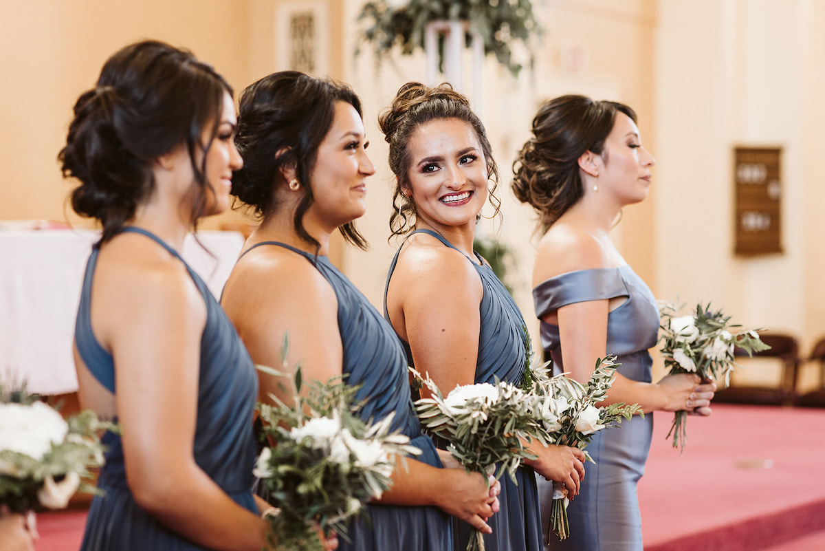 bridesmaids hold simple bouquets of white flowers and greenery and smile at the front of the church