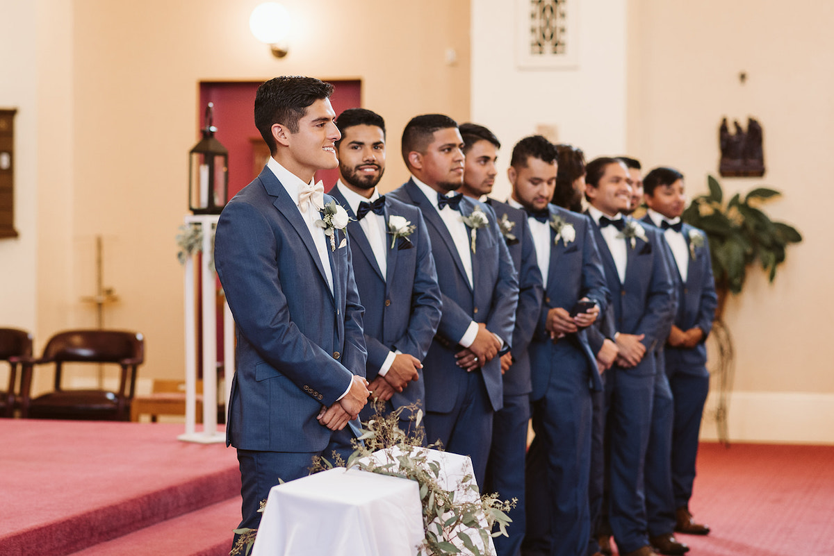 groom and groomsmen stand at the altar with their hands crossed in front of themselves