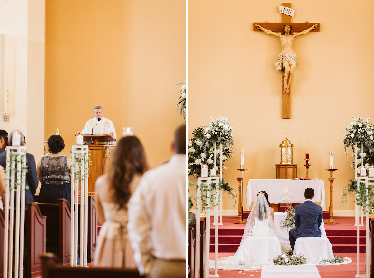 priest presents a reading as wedding guests stand. bride and groom sit at altar under the crucifix