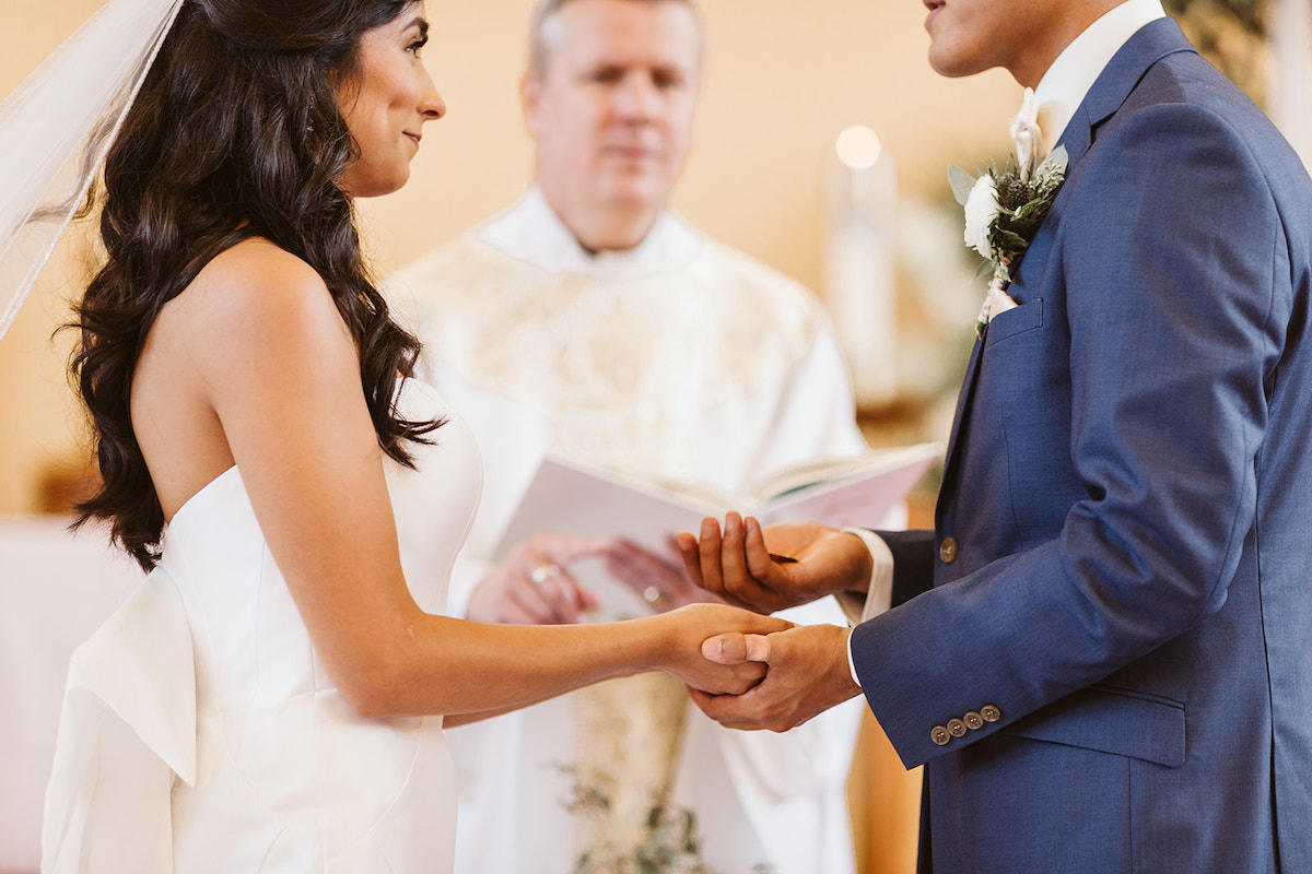 Bride and groom smile at each other and hold hands before priest