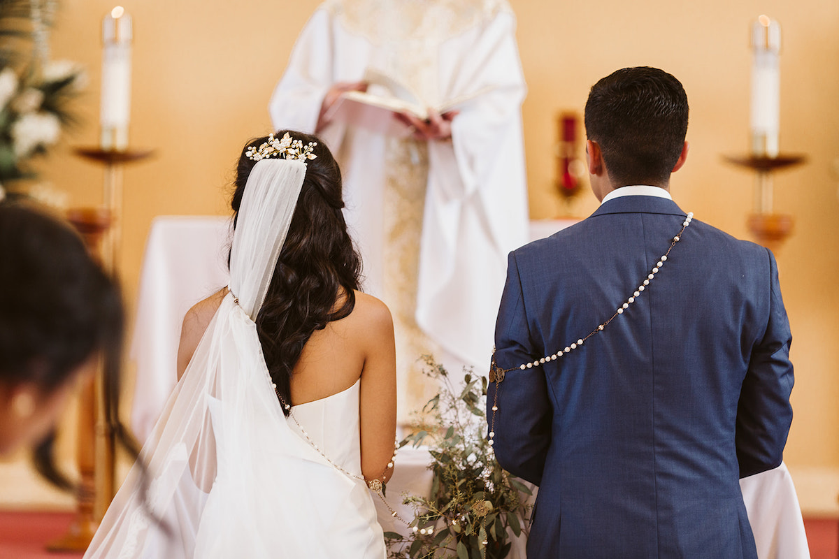Large wedding lasso rosary over bride and groom shoulders as they listen to priest