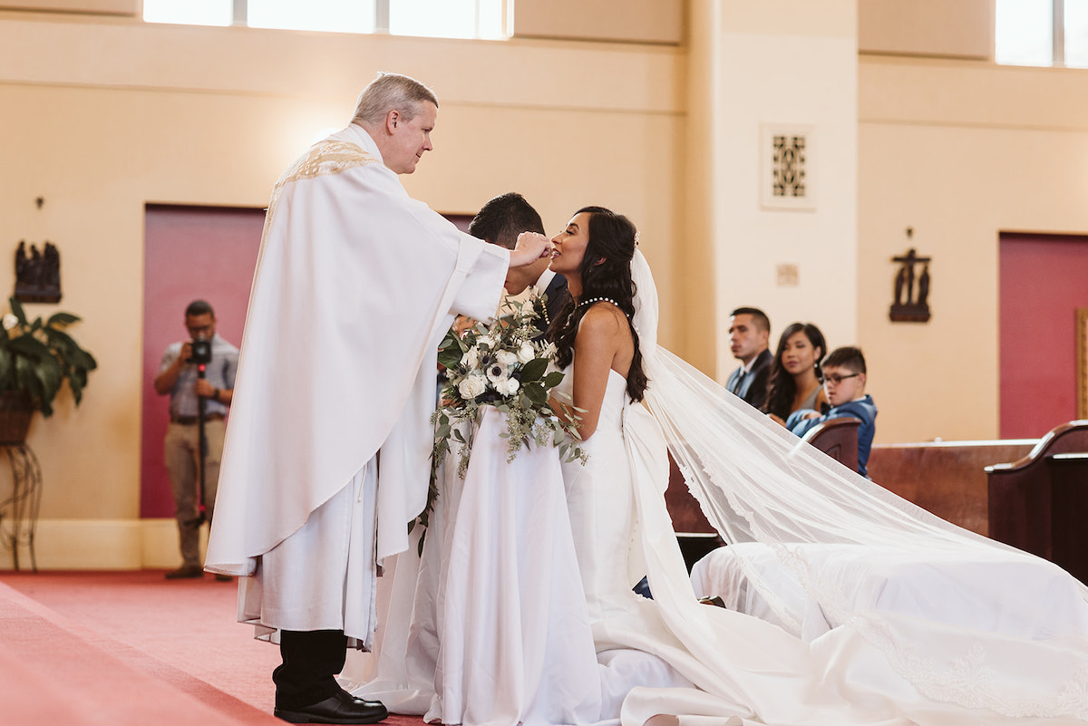 priest places communion bread on brides tongue
