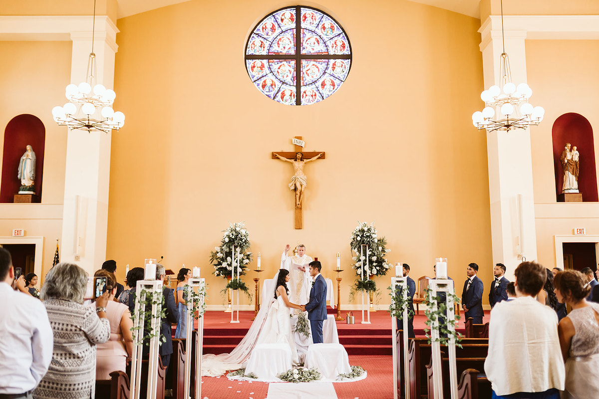 bride and groom hold hands and face each other under the crucifix and stained glass window at St Josephs Catholic Church in Dalton Georgia