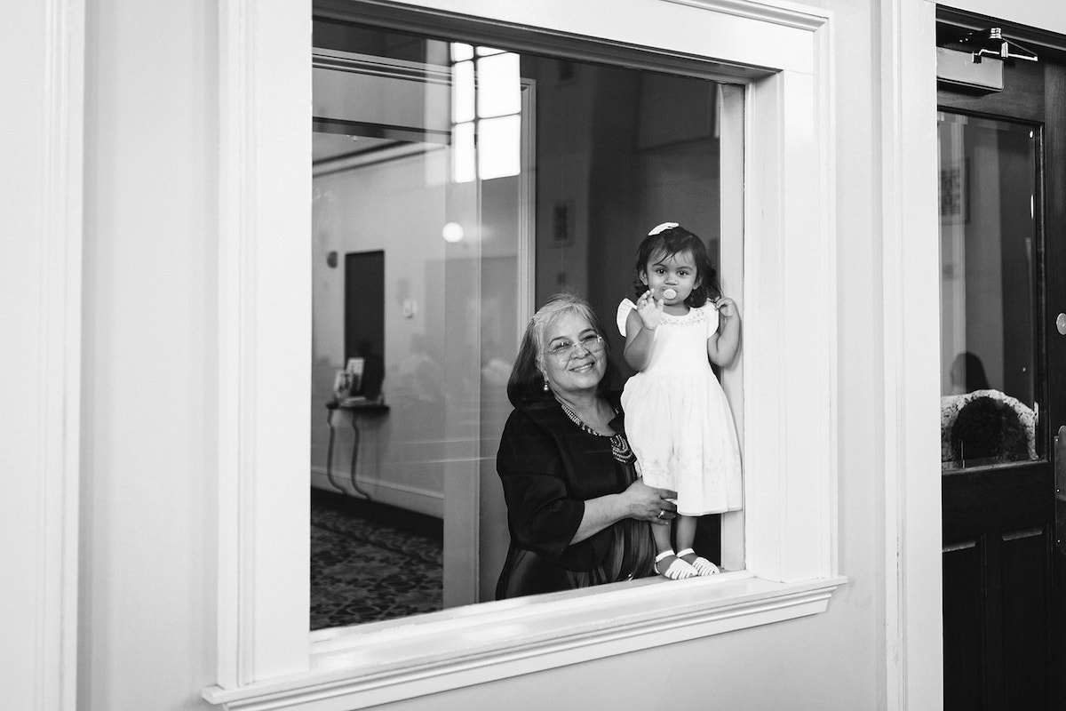 older woman holds a small toddler girl behind a large glass window at St Josephs Catholic Church wedding