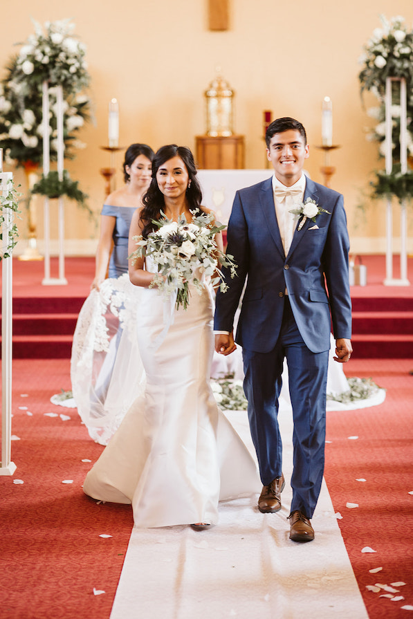 bride and groom hold hands and smile as they walk from the altar during recessional