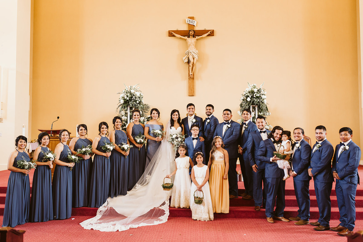 wedding party poses together on altar steps beneath the crucifix