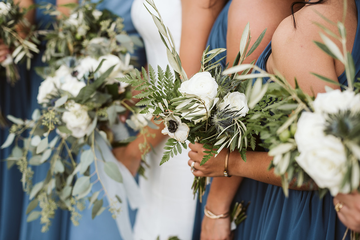 bridesmaids bouquets of white flowers and greenery contrast with their cornflower blue dresses
