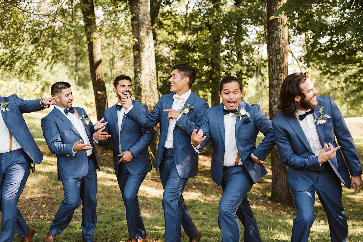 groom and groomsmen in cornflower blue suits and bowties laugh and point at each other