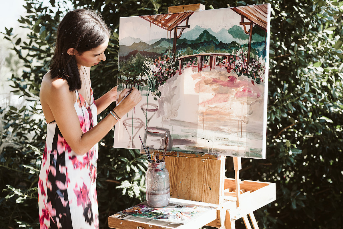 woman paints watercolor scenery at an easle
