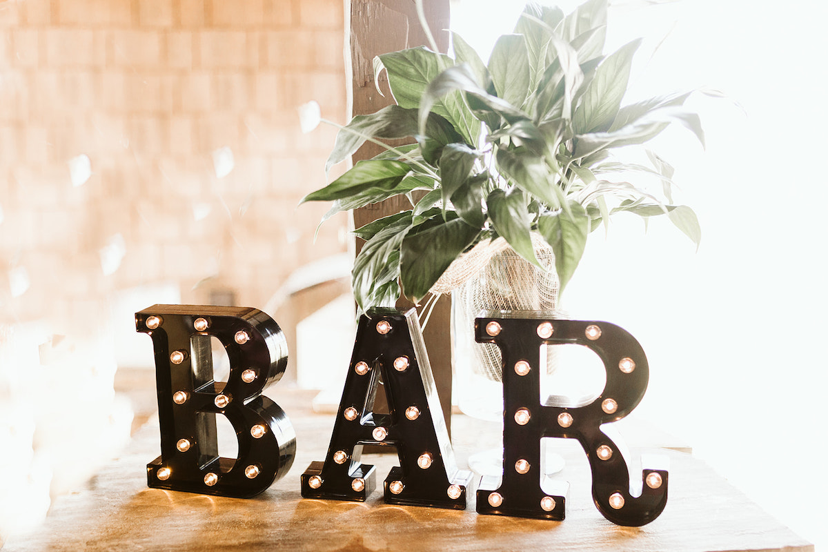 BAR sign lit with small white lightbulbs on a table near a green plant