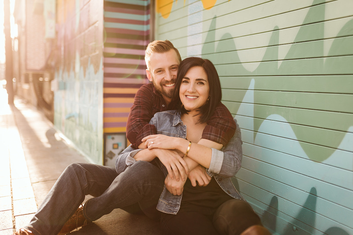 man and woman sit against a painted wall in Denver's RiNo art district for engagement photos